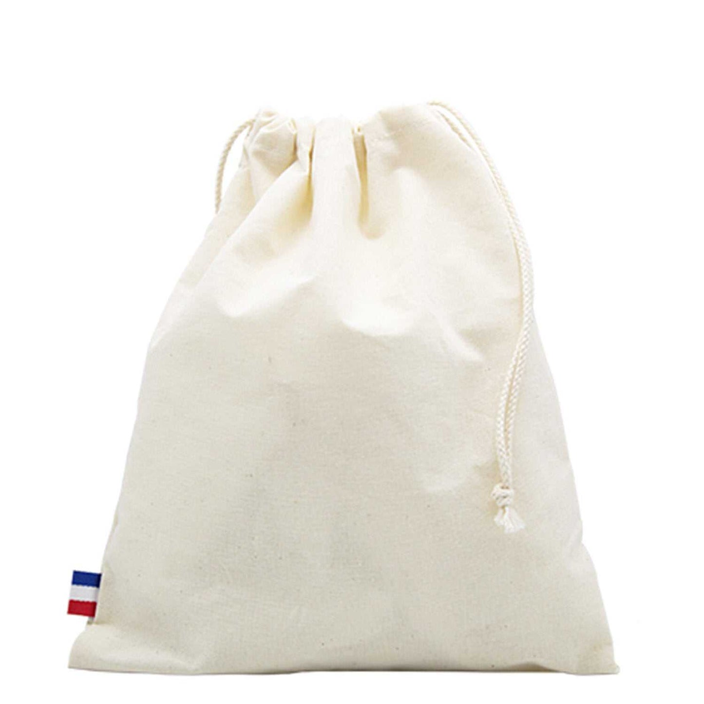 Sac de plage en coton biologique GOTS, grand format, posé sur une serviette au bord de la mer avec accessoires de plage (lunettes, livre, crème solaire)