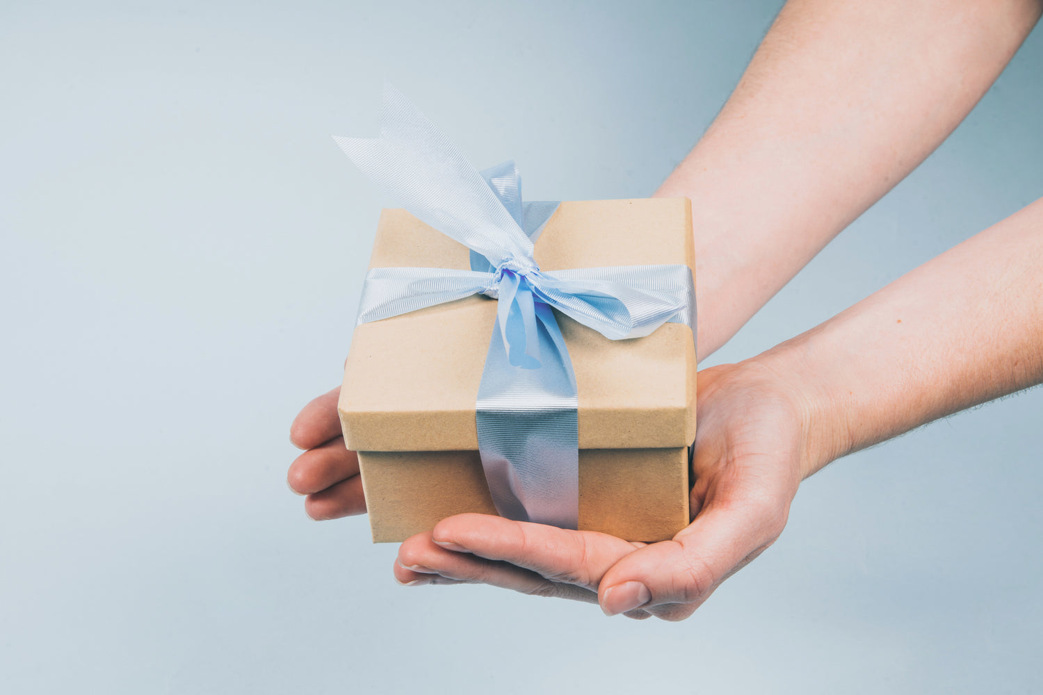 Petite boîte cadeau en carton kraft avec ruban bleu tenue dans les mains, idée d’offrir un sac