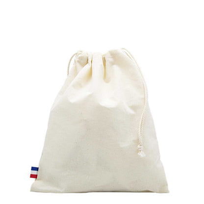 Sac de plage en coton biologique GOTS, grand format, posé sur une serviette au bord de la mer avec accessoires de plage (lunettes, livre, crème solaire)

