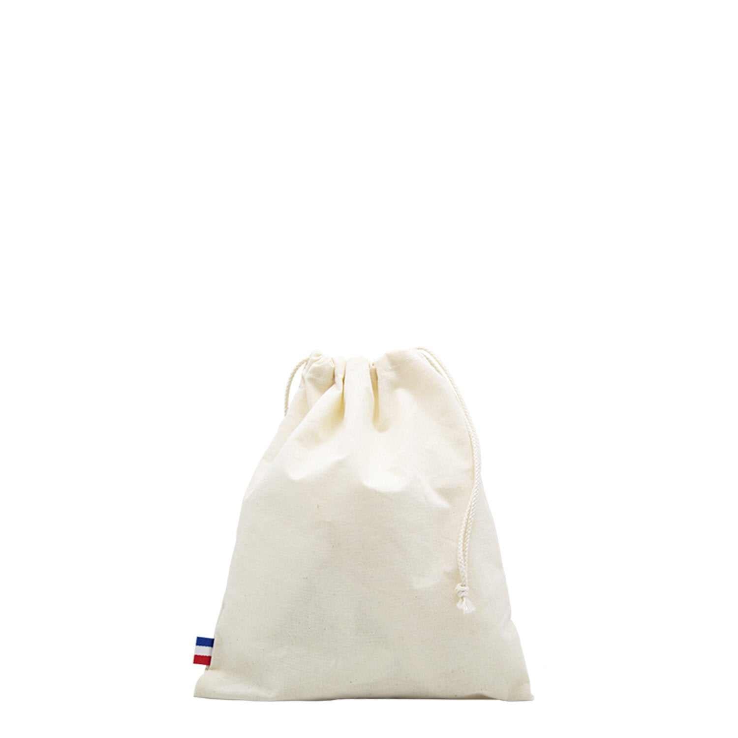 Sac de plage en coton biologique GOTS, grand format, posé sur une serviette au bord de la mer avec accessoires de plage (lunettes, livre, crème solaire)

