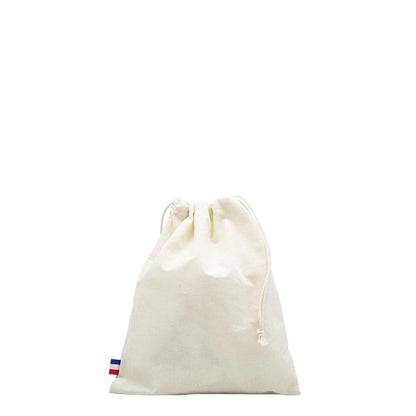 Sac de plage en coton biologique GOTS, grand format, posé sur une serviette au bord de la mer avec accessoires de plage (lunettes, livre, crème solaire)

