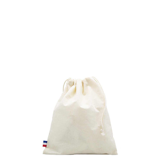 Sac de plage en coton biologique GOTS, grand format, posé sur une serviette au bord de la mer avec accessoires de plage (lunettes, livre, crème solaire)

