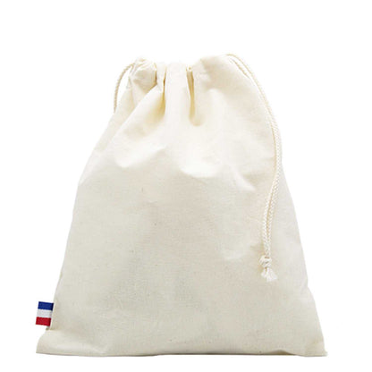 Sac de plage en coton biologique GOTS, grand format, posé sur une serviette au bord de la mer avec accessoires de plage (lunettes, livre, crème solaire)

